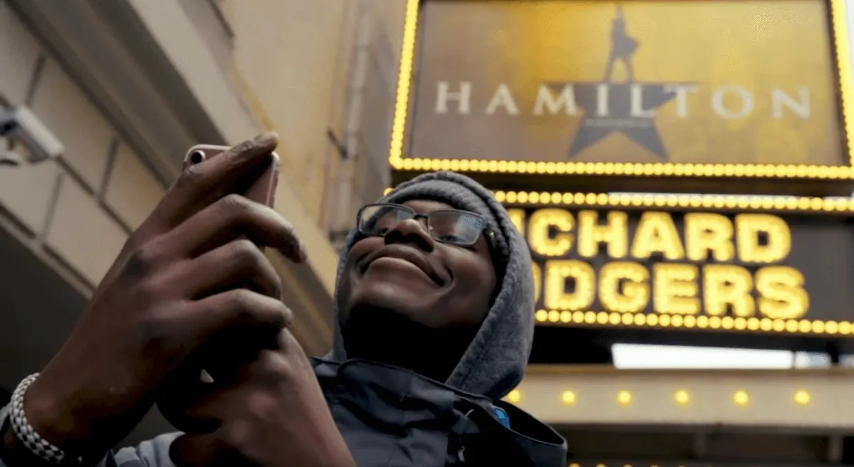 A fan holding up a phone under the Hamilton marquee at the Richard Rodgers Theatre