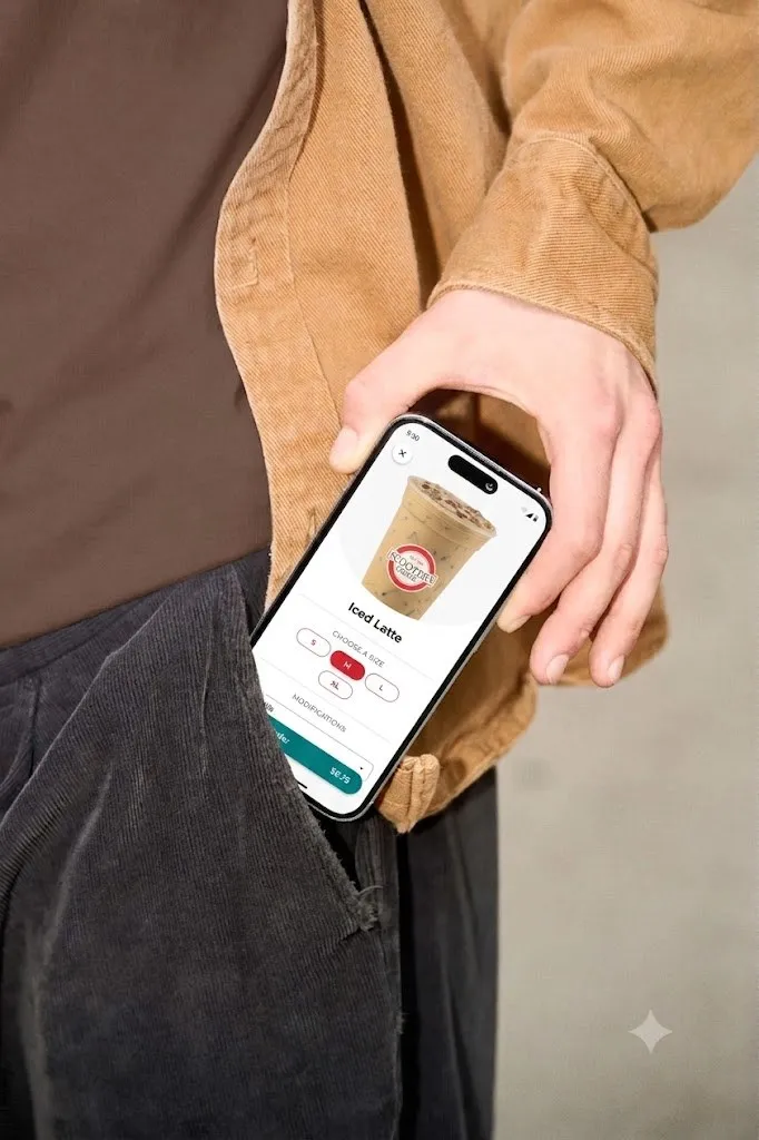 A hand pulling a phone from a pocket with the Scooter’s Coffee app open on an iced latte
